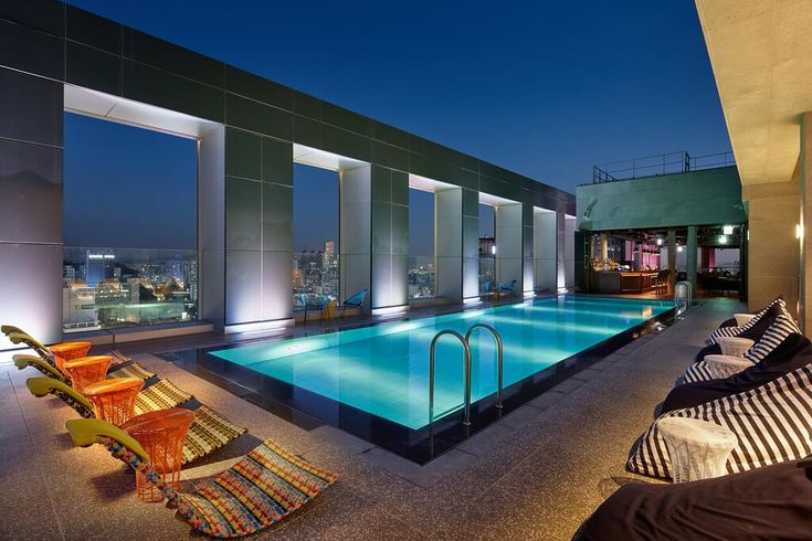 an indoor swimming pool in the middle of a rooftop with lounge chairs and large windows