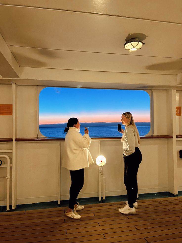 two women standing on the deck of a ship looking out at the ocean and taking pictures