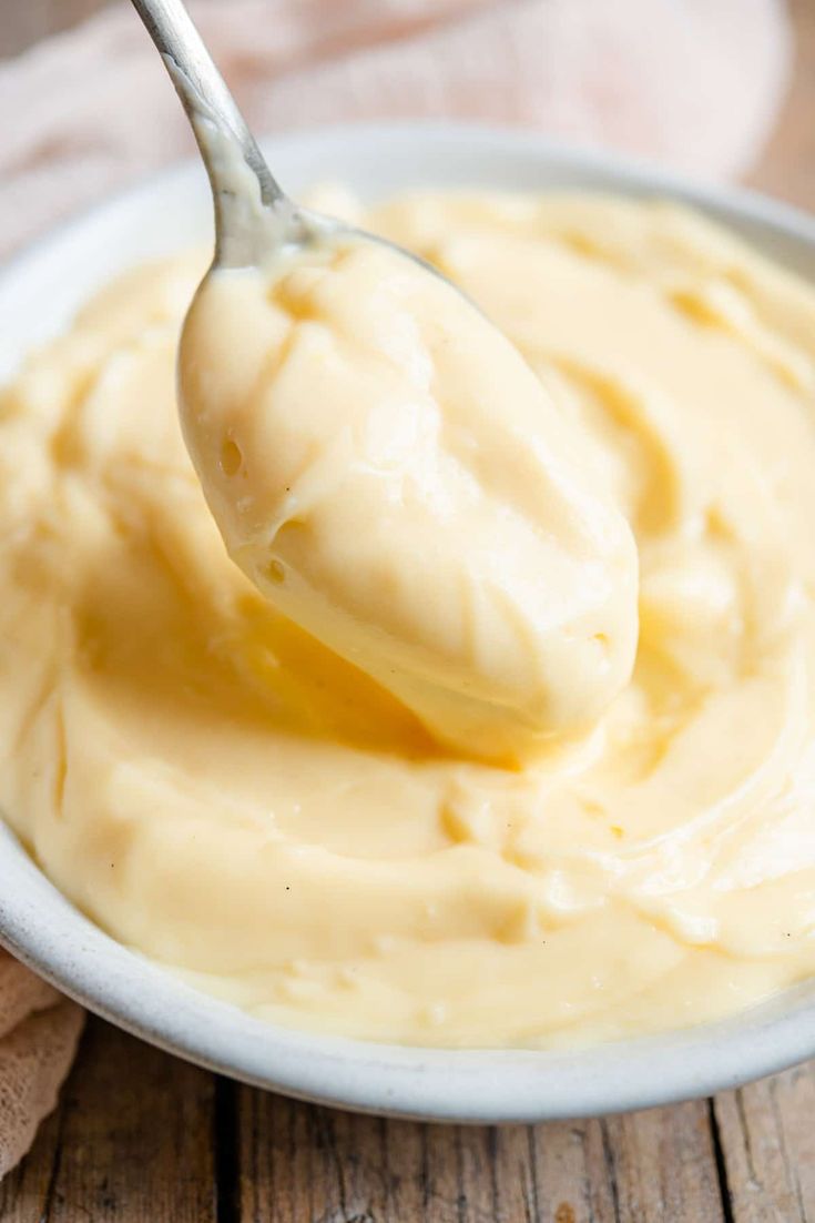 a spoon full of mayonnaise sitting on top of a white bowl filled with sauce