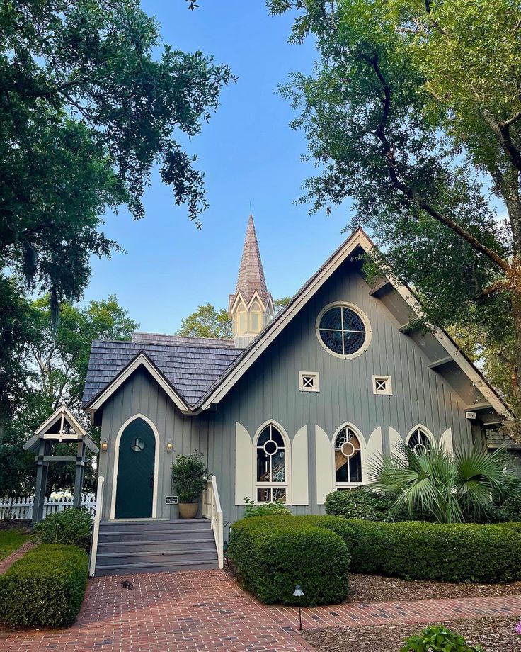 a gray and white house with a steeple on the top, surrounded by greenery