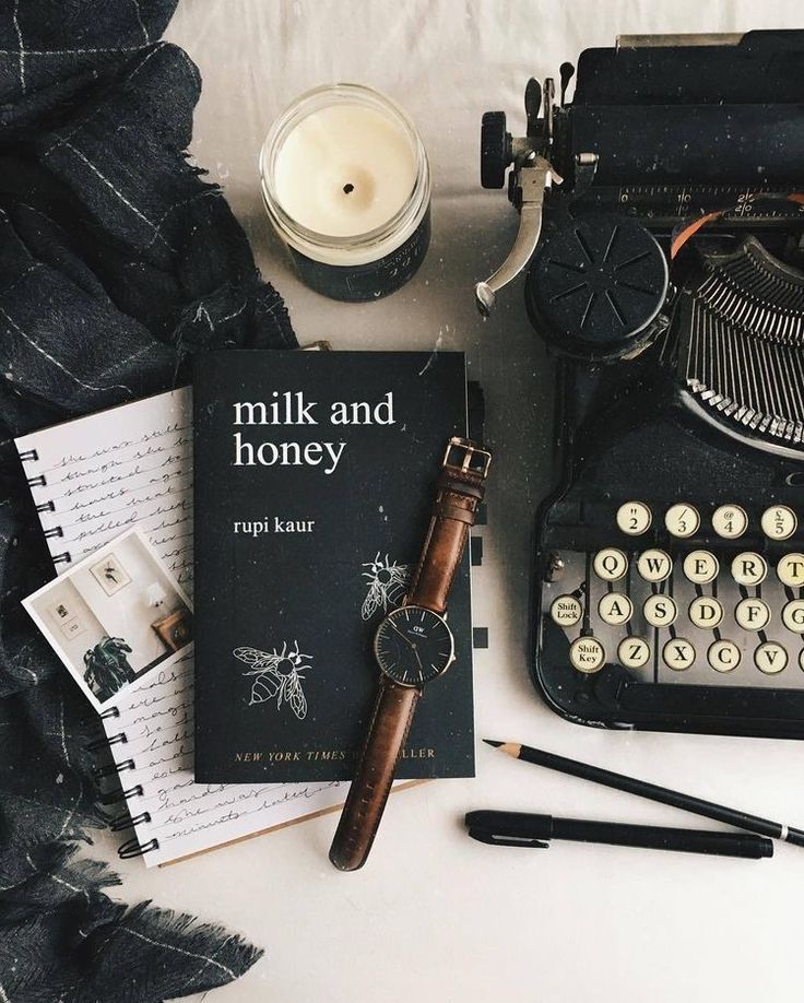 an old fashioned typewriter sitting on top of a bed next to other books and writing utensils