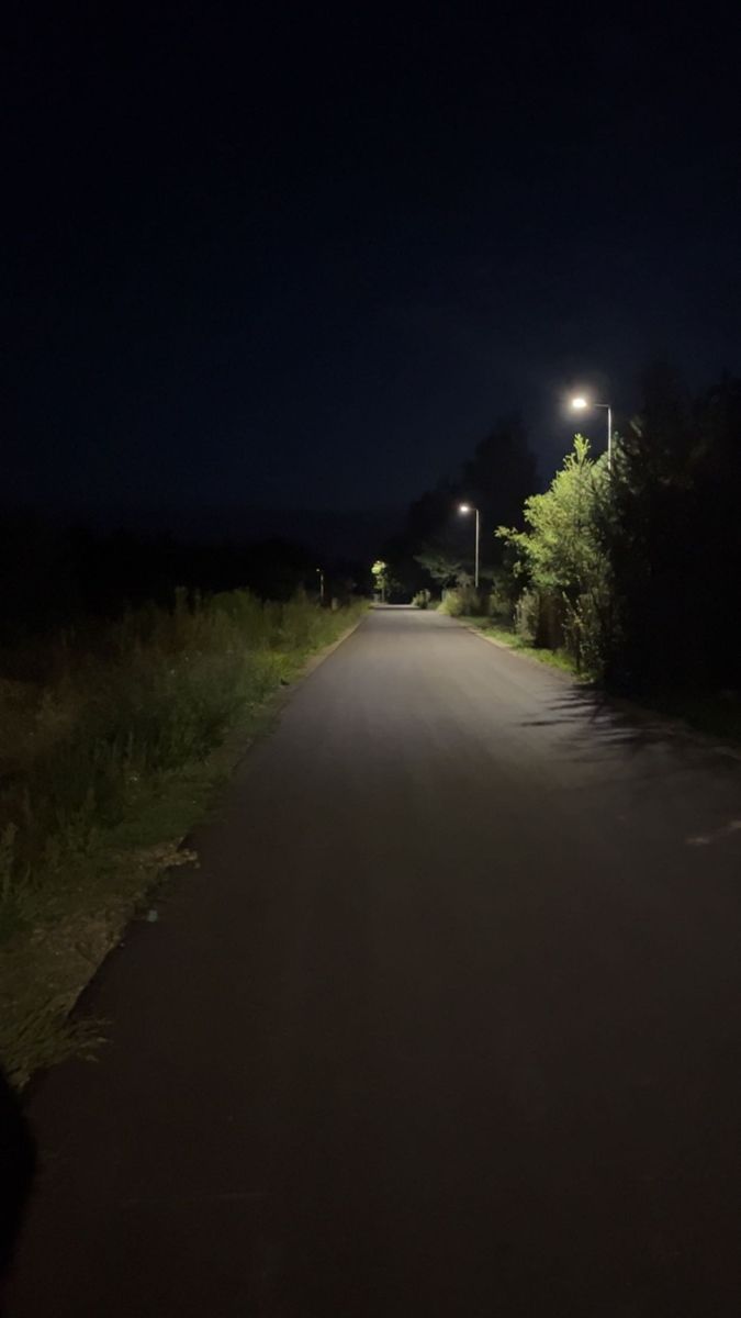 an empty road at night with street lights on the side and trees in the background