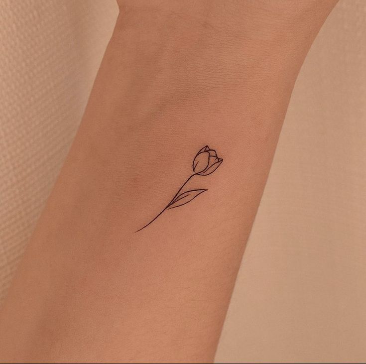 a single flower tattoo on the wrist is shown in black ink and has a thin outline