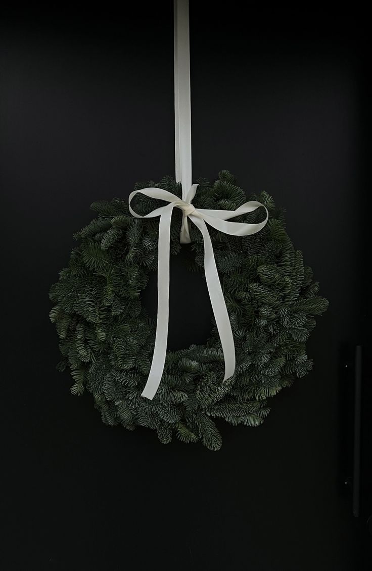 a christmas wreath hanging from the side of a door with a white ribbon on it