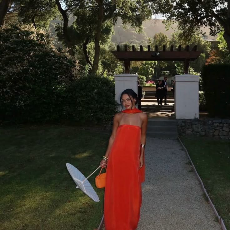 a woman in an orange dress is standing outside