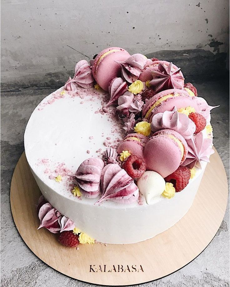 a white cake with pink frosting and strawberries on top is sitting on a wooden platter