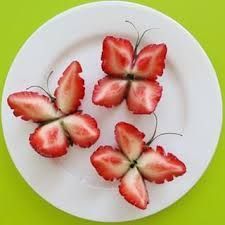 four strawberries arranged in the shape of butterflies on a white plate against a green background