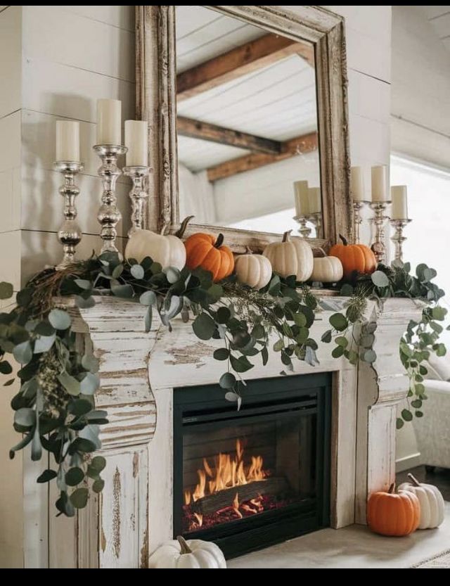 a fireplace with candles, pumpkins and greenery on it in front of a mirror