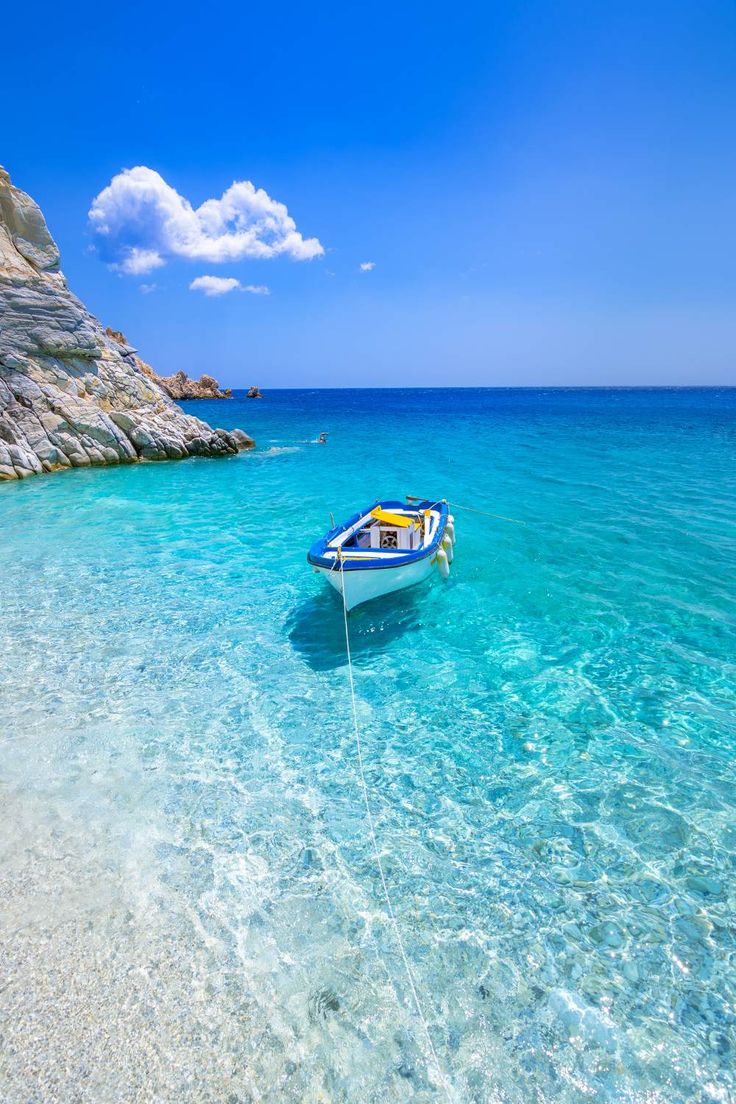 a small boat floating on top of a blue ocean next to a rocky cliff face