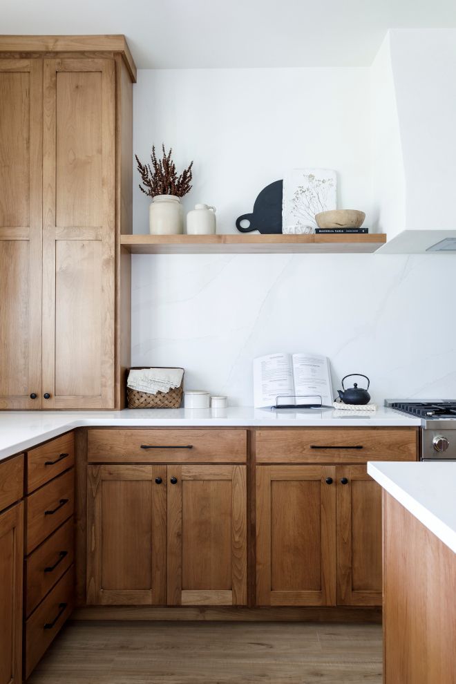 a kitchen with wooden cabinets and white counter tops, open bookshelf above the stove