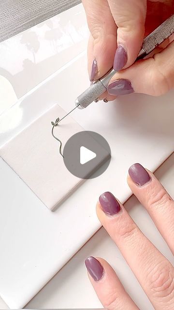 a woman with purple nail polish on her nails is using a needle to cut something