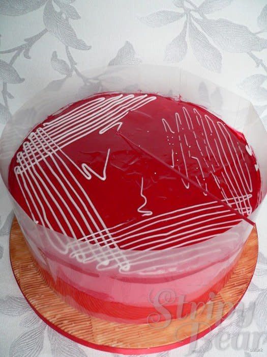 a red cake sitting on top of a wooden platter covered in plastic wrapper