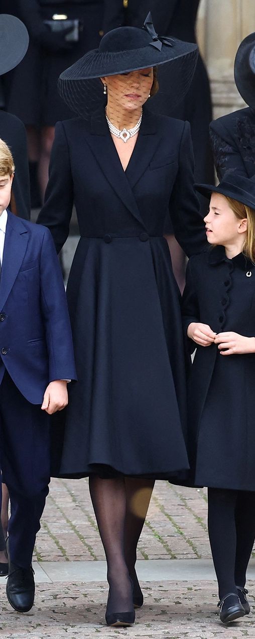 a woman in a black dress and hat walking with two children