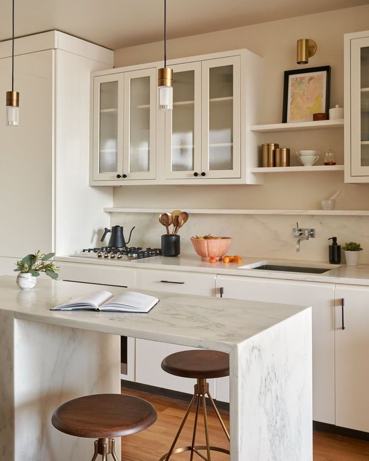 a kitchen with white cabinets and marble counter tops, two stools in front of the island