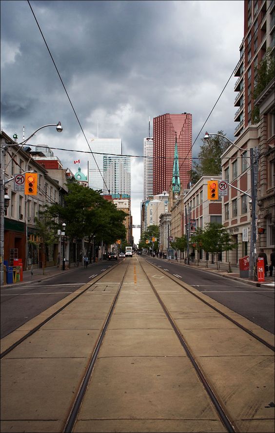 an empty city street with buildings and traffic lights in the distance on a cloudy day