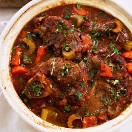 a white bowl filled with meat and vegetables on top of a table next to bread