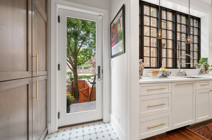 a kitchen with white cabinets and wood flooring next to an open door that leads to a patio