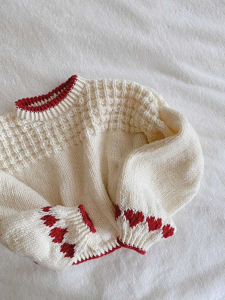 a white sweater with red hearts on it laying on top of a bed next to a pillow