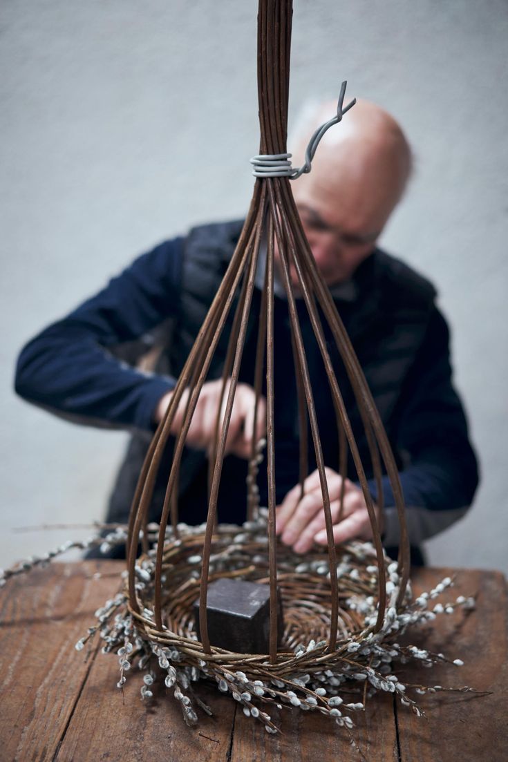 a man sitting at a table in front of a birdcage filled with twigs