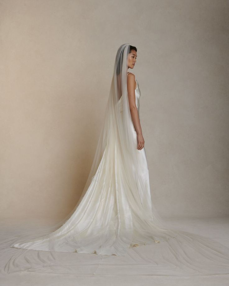 a woman in a white wedding dress with a veil on her head standing against a wall