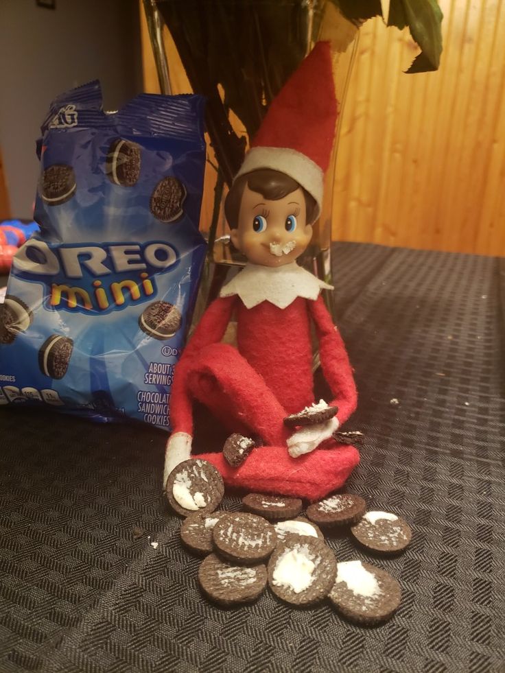 an elf is sitting on the table next to some coins and a bag of oreo mints