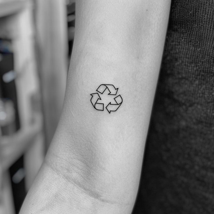 a black and white photo of a woman's arm with a recycle tattoo on it