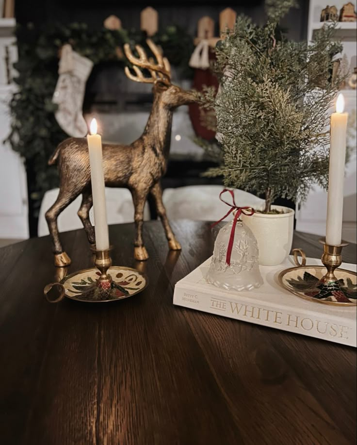 two candles are sitting on a table next to a deer figurine and a christmas tree