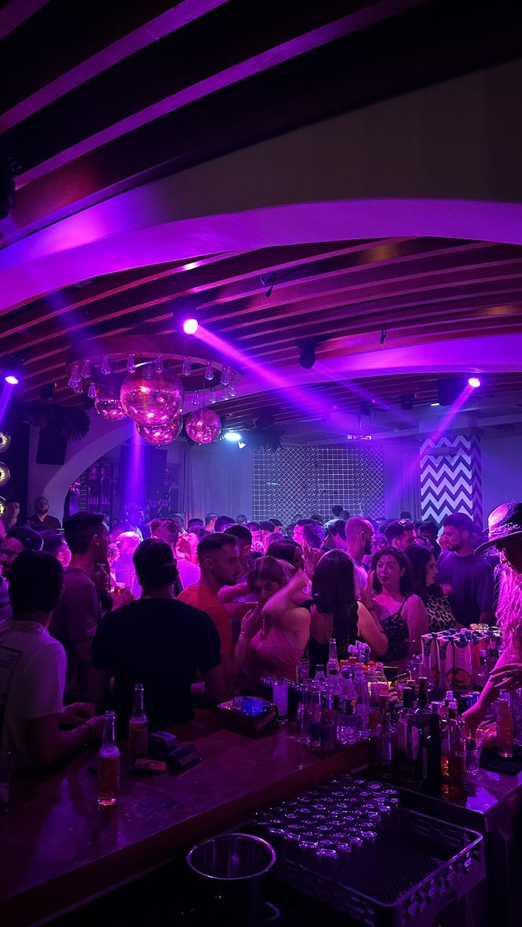 a group of people sitting at a bar with purple lights