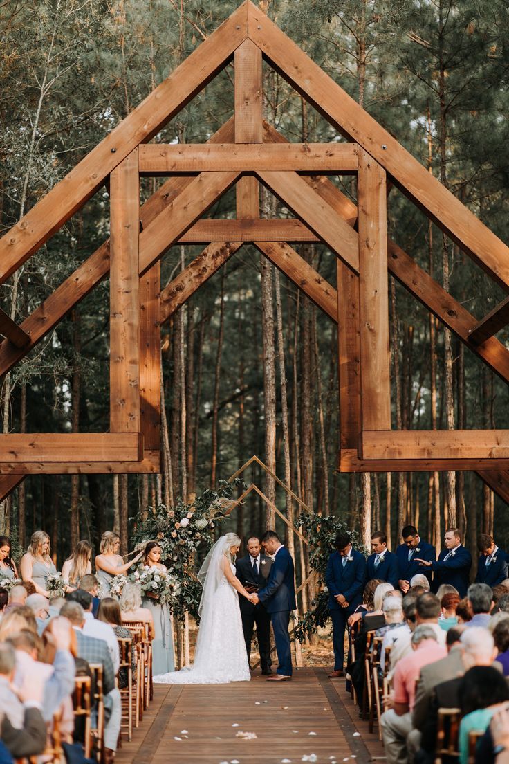 a bride and groom standing at the end of their wedding ceremony under a wooden structure