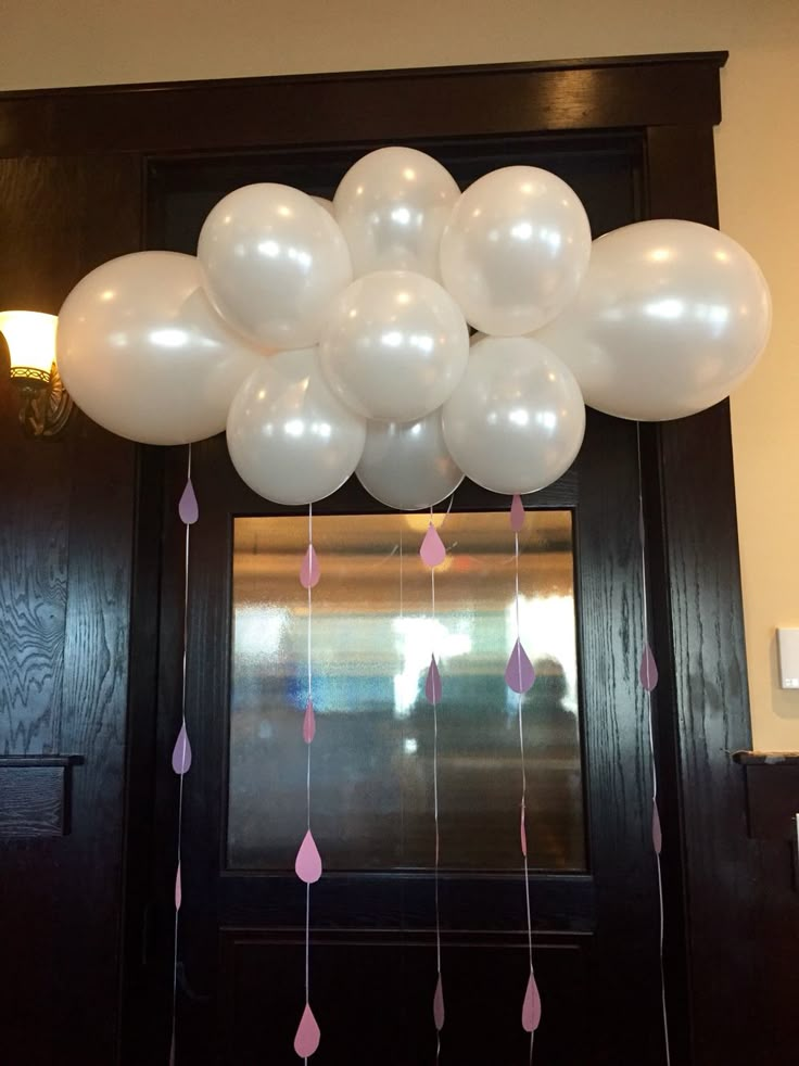 a bunch of white balloons hanging from the ceiling in front of a door with pink tassels