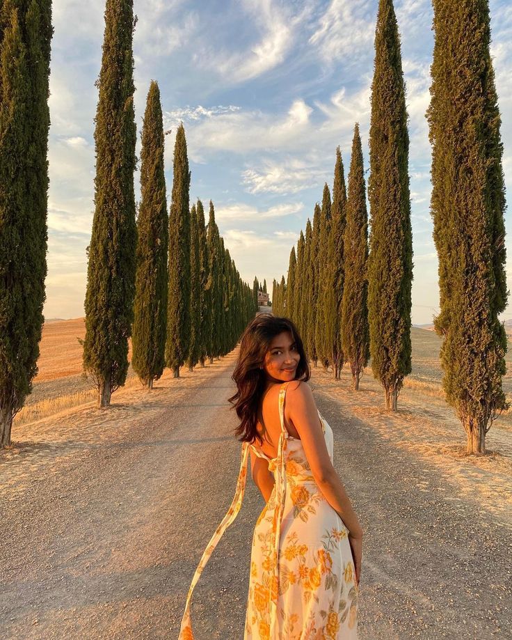 a woman standing in the middle of an empty road with trees lining both sides and behind her