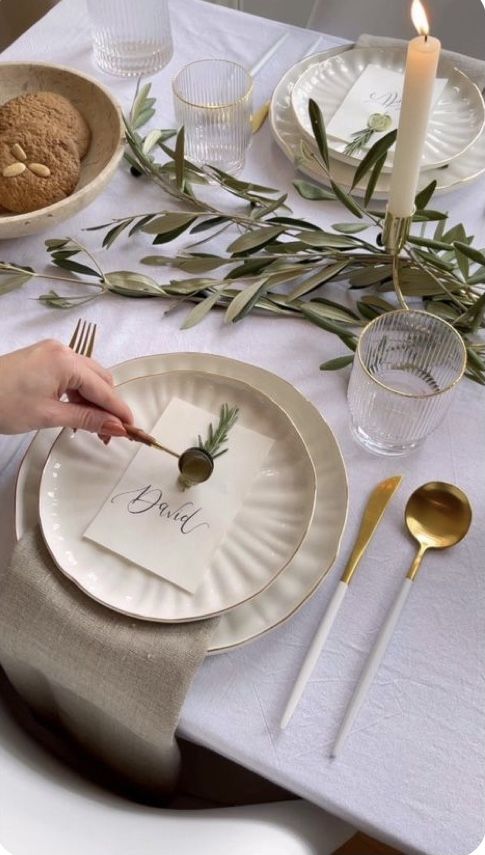 a table set with plates, silverware and napkins for an olive centerpiece