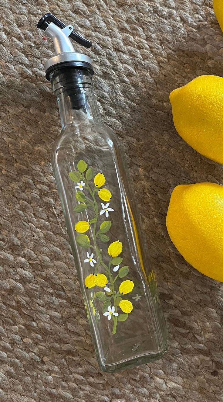 a glass bottle with yellow flowers painted on it next to lemons