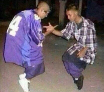 two young men are dancing together in the street at night, one is wearing an oversized purple jacket