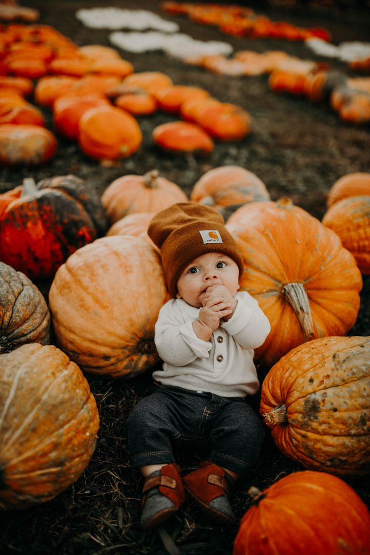 a baby sitting on the ground surrounded by lots of pumpkins and other small ones