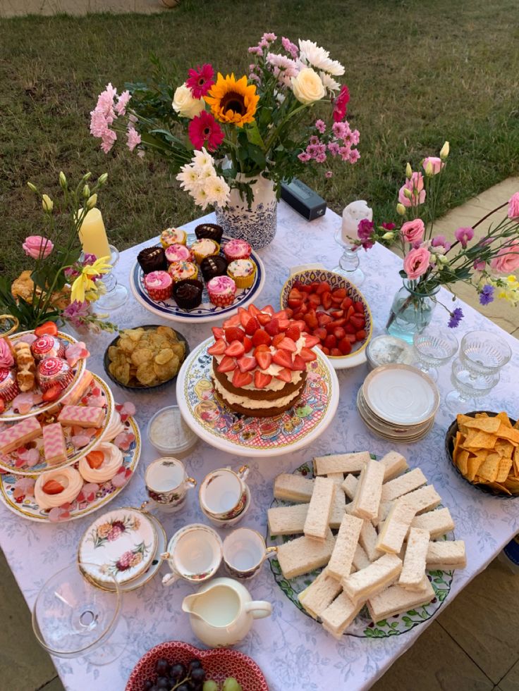 a table topped with lots of food on top of a lush green field next to flowers