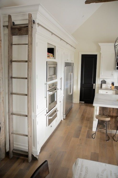 a kitchen with white walls and wooden floors, an oven in the center is next to a ladder