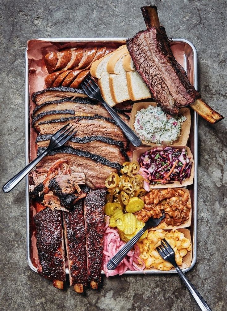 an assortment of meats and sides on a tray with utensils next to them