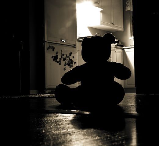 a black and white photo of a teddy bear sitting on the floor in a kitchen