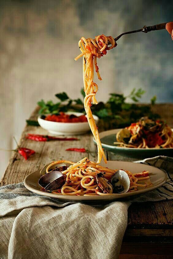 spaghetti being lifted from a plate by tongs on a wooden table with other dishes in the background