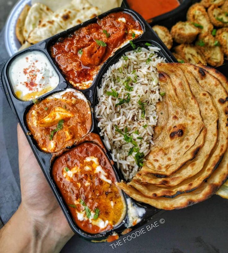 a person holding a tray full of food with rice, naan bread and sauces