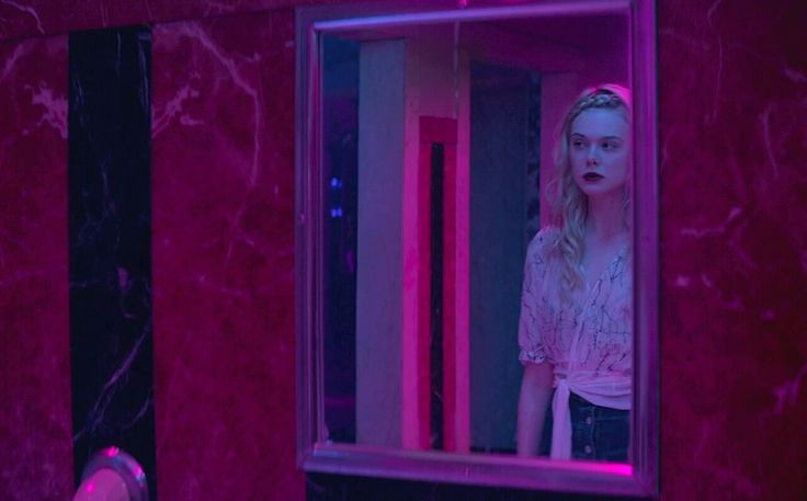 a woman standing in front of a mirror looking into the room with red light coming from it