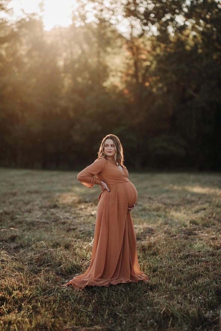 a pregnant woman in an orange dress poses for the camera with her hands on her hips