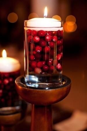 a candle is filled with cranberries on a table