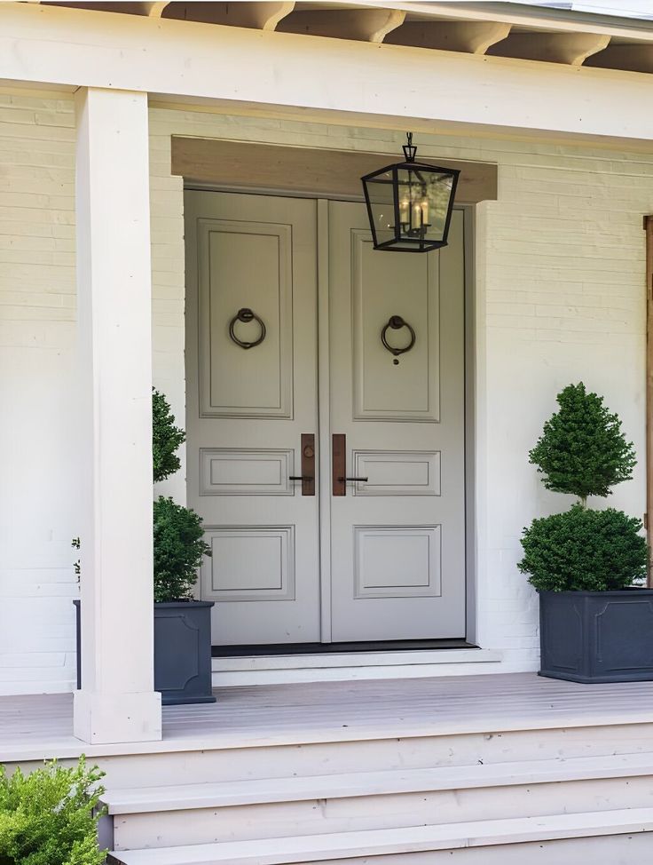 two potted plants sit on the front steps of a white house with double doors