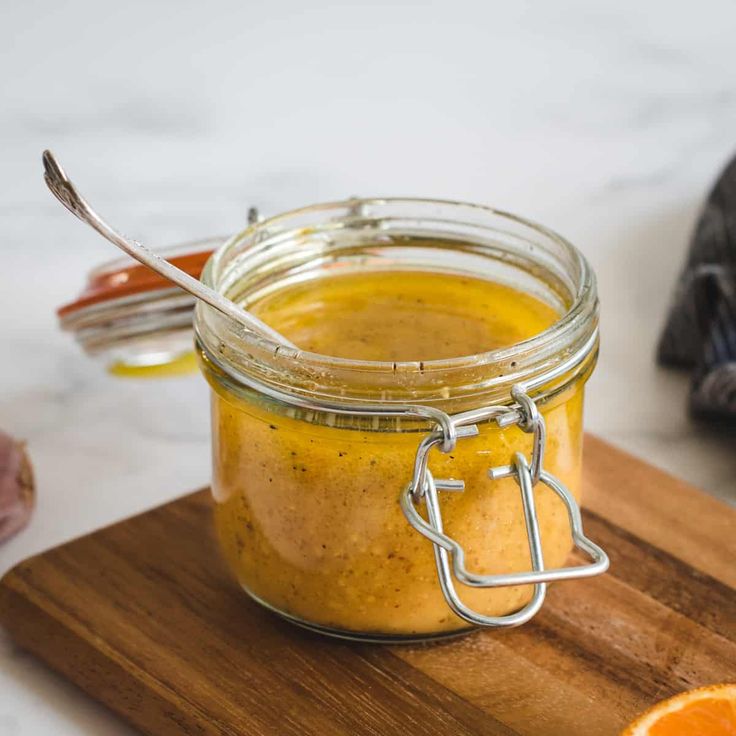 an orange is sitting on a cutting board next to a jar of mustard with a spoon in it