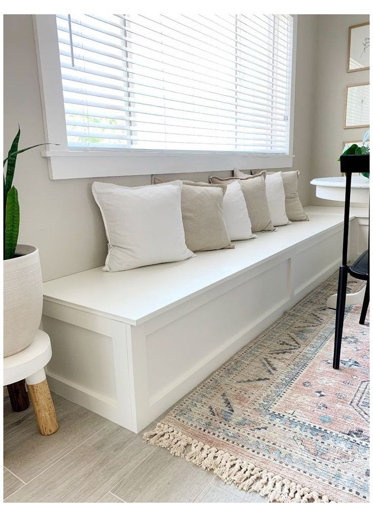 a white bench sitting in front of a window next to a table with a potted plant on it