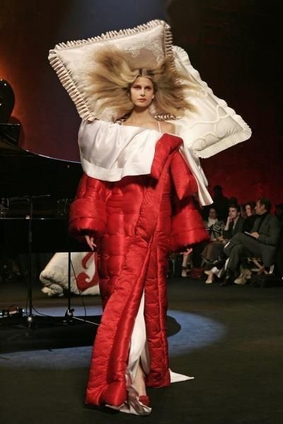 a woman in a red and white dress with a large pillow on her head at a fashion show