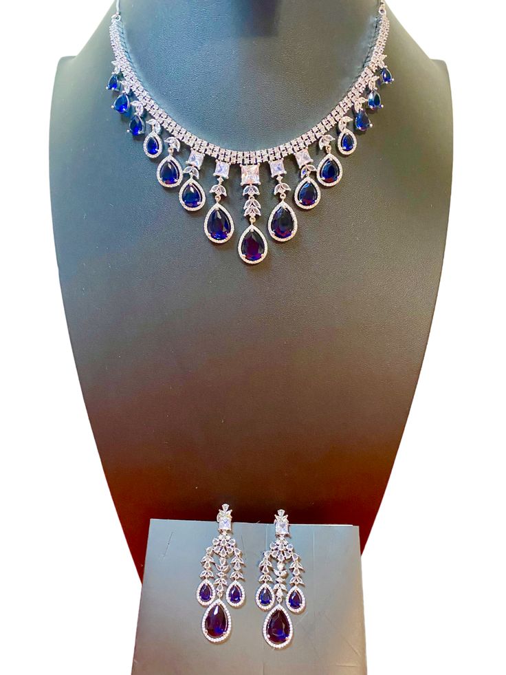 Add some sparkle to any occasion with our CZ American Diamond Necklace. Perfect for weddings, parties, or as a gift for her. This stunning necklace, made with beautiful bluestones, will elevate any outfit like sarees, gowns, or lehengas. Make a statement with this beautiful and versatile piece. This jewellery set includes a necklace and matching earrings. Jewellery Care- Keep the jewellery dry, avoid contact with perfumes and water. Elegant Blue Necklace For Reception, Elegant Blue Necklace For Receptions, Bollywood Blue Bridal Necklace Hand Set, Blue Bollywood Jewelry For Reception, Blue Bollywood Necklace For Receptions, Blue Hand Set Bridal Necklace For Celebration, Blue Bridal Necklace Hand Set For Celebrations, Blue Hand-set Bridal Necklace For Celebration, Elegant Blue Necklace With Stone Work