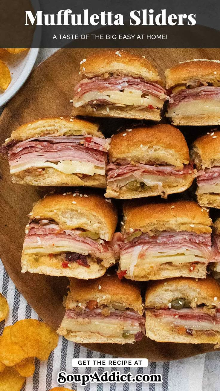 a pile of sandwiches sitting on top of a wooden cutting board next to potato chips